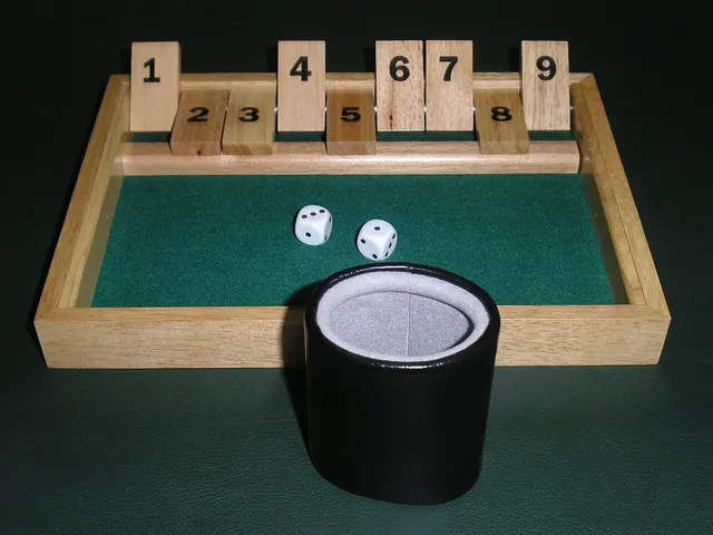 A classic wooden Shut the Box with tiles 2, 3, 5 and 8 flipped down, two dice on the felt and a leather dice cup