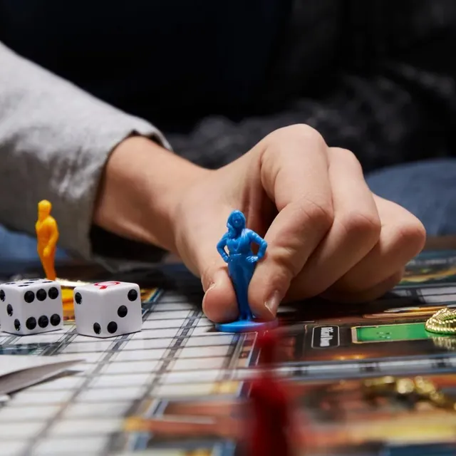 A hand moving a blue pawn across the board, with dice nearby