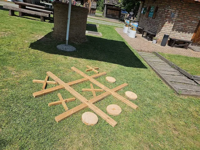 A giant tic-tac-toe made of wooden planks and round wooden discs on a lawn