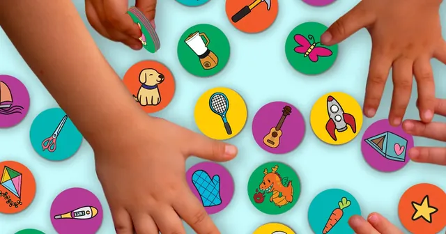 Several hands grabbing round picture tokens spread over a table
