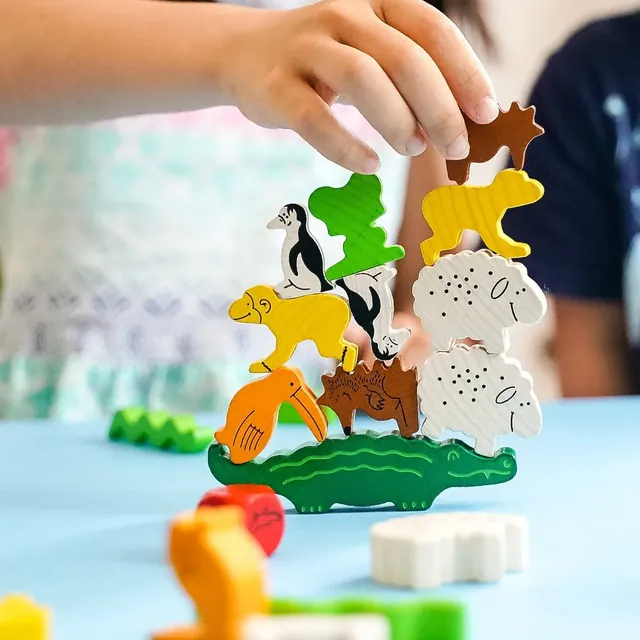 A child's hand placing a brown animal on top of a wobbly pile
