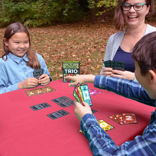 A woman and two children playing Trio at an outdoor table, with matched cards laid out in front of them