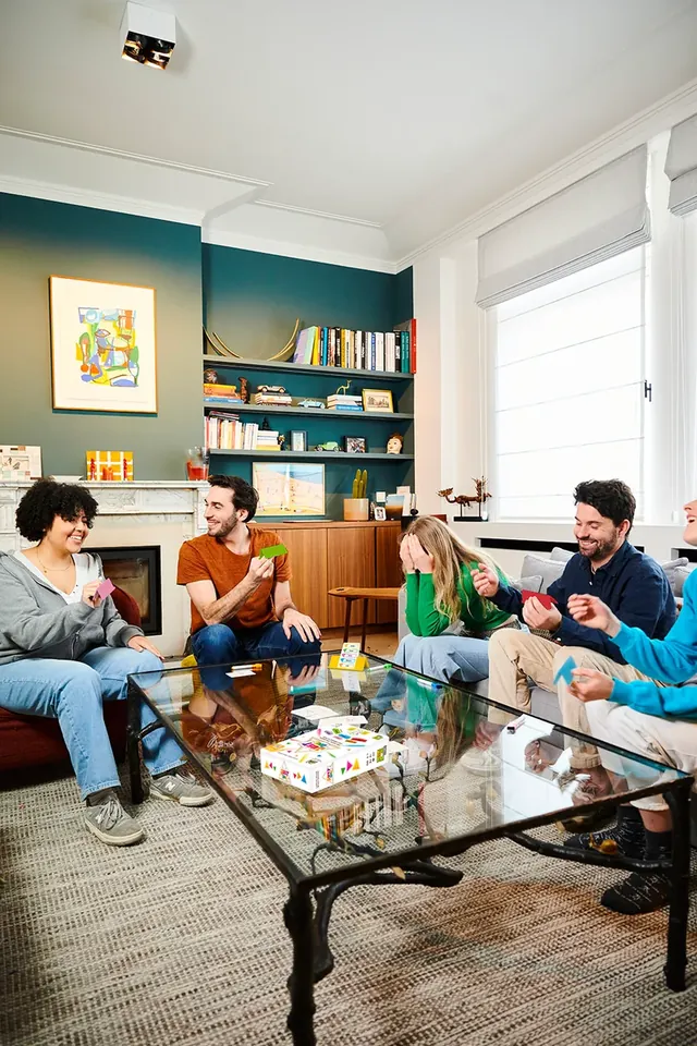 A group of six friends playing Just One around a glass coffee table