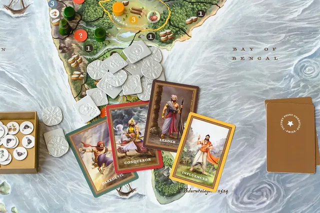 White embossed coins and a tray of round tokens on the southern tip of the map by the Bay of Bengal, with four illustrated personality cards (Daredevil, Conqueror, Leader, Influencer) and the victory-point prize deck