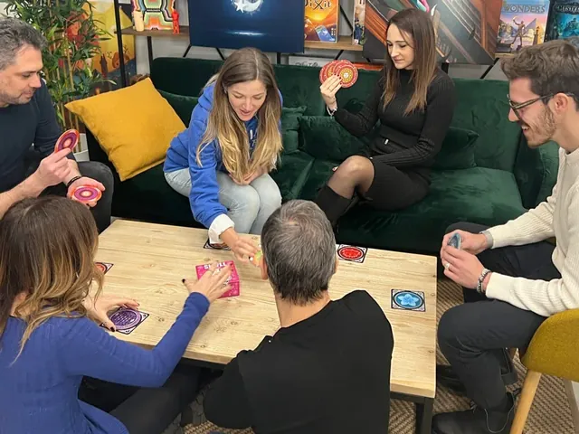 Six friends on sofas around a coffee table, holding Skull discs and making bids