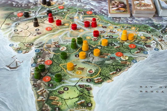 Close-up of the map of northern and central India with tall wooden army pieces and round wooden forts in red, yellow, green and black spread across the regions, plus orange question-mark tokens and resource symbols