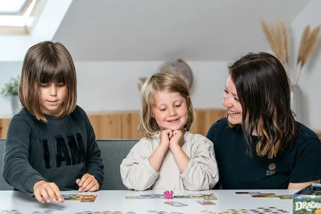 Two young girls and a woman playing Dragomino at a table