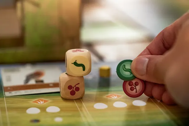 A hand taking a food token next to two wooden dice showing fruit and grain