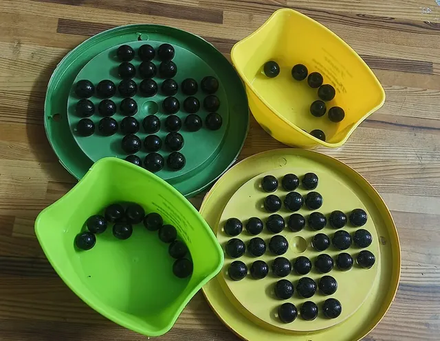 Plastic Brainvita boards and trays in green and yellow, with black marbles
