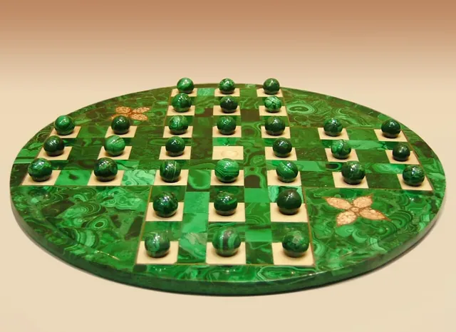 An oval peg solitaire board of green semi-precious stone with matching marbles