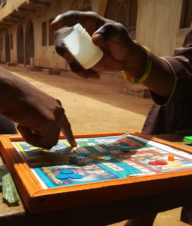 Hands rolling the die from a cup over a Ludo board on a small wooden table