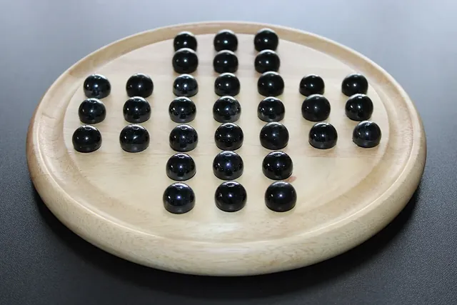 A round wooden peg solitaire board with black marbles, a few holes already empty