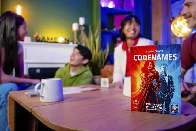 Friends laughing on a sofa during a game, with the Codenames box on the table