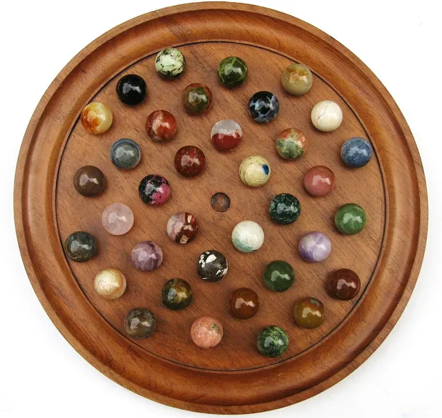 A French-style wooden solitaire board filled with stone marbles of different colours