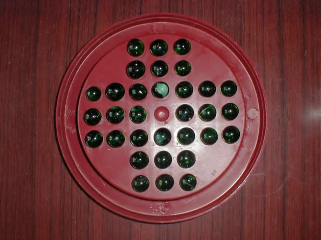 A red plastic Brainvita board with green glass marbles in 32 of its 33 holes and the centre hole empty