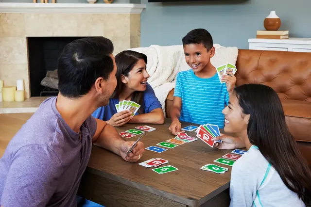 A family of four playing Skip-Bo around a wooden table