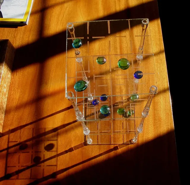 A clear acrylic 3D tic-tac-toe with stacked grids and glass marbles