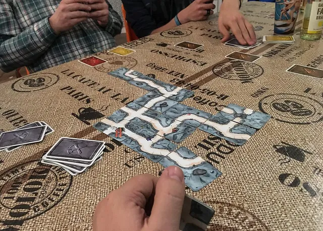 Players' hands over a winding tunnel of Saboteur path cards laid across a table